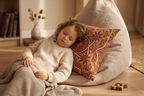 Child sleeping on a bean bag chair with a pillow and blanket in a cozy room.